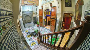 A narrow, ornate corridor with intricate tile work, a wooden staircase, and a small seating area with a table and chairs. - Riad Dar Fes (Fes)
