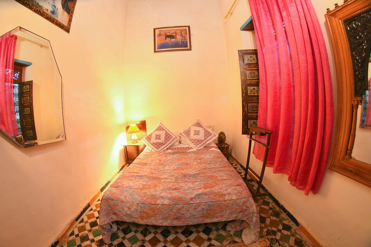 A bedroom with a bed, a nightstand, a lamp, a mirror, and a window with curtains.