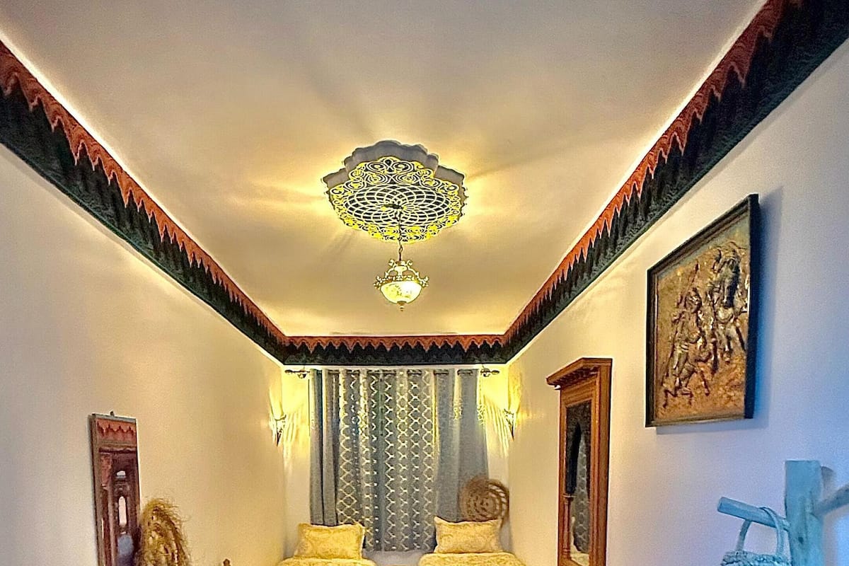 A room with two beds, a red sofa, patterned rugs, and a decorative ceiling light.