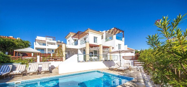 A modern two-story house with a swimming pool, outdoor seating, and a pergola.
