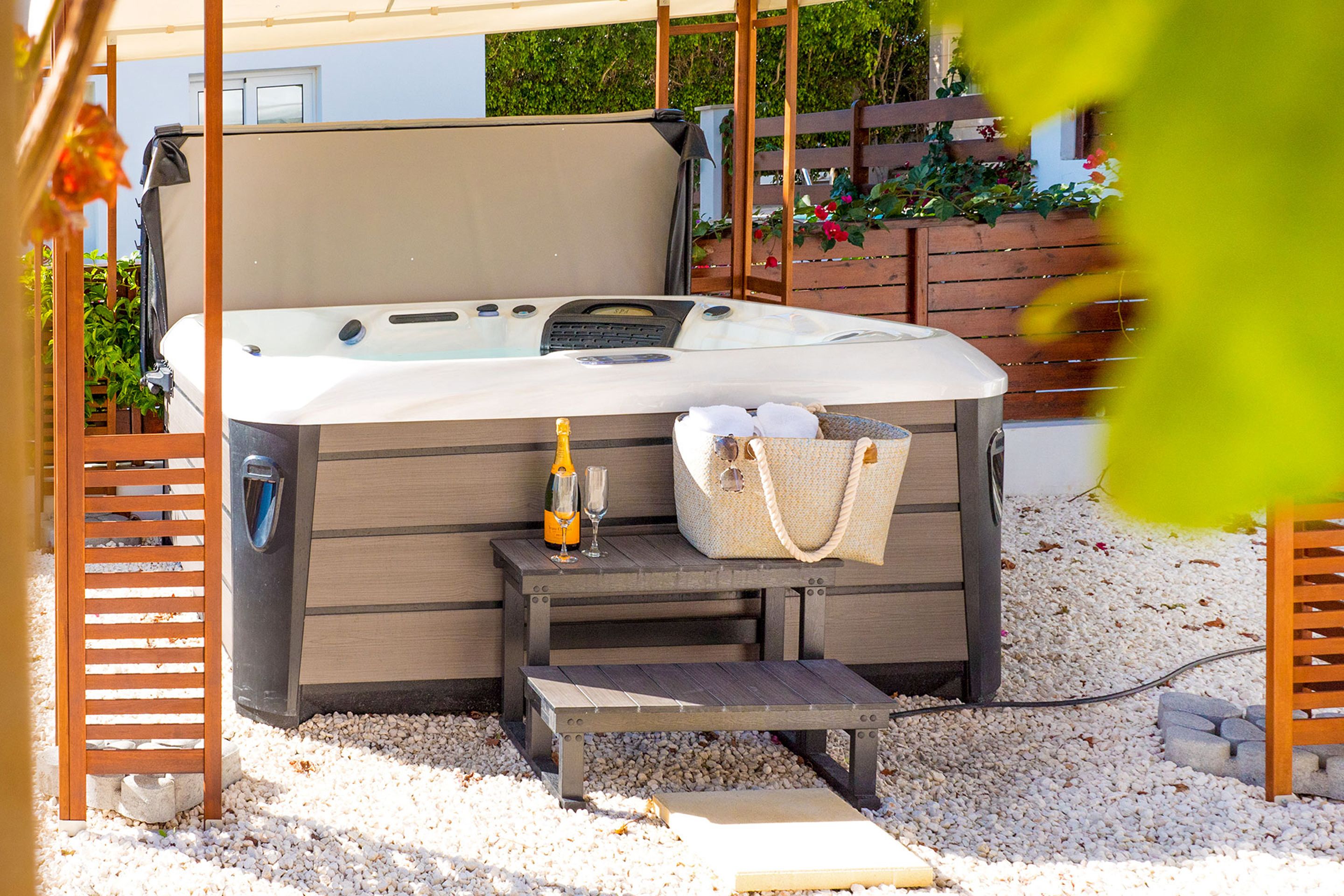 A hot tub with a wooden bench, a bottle of champagne, and a handbag on the side.