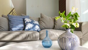 A living room with a beige sofa, a blue vase with white flowers, and a blue glass vase on a white table. - Villa Porto (Pegeia)
