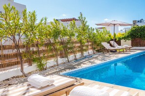 Una piscina al aire libre, sombrillas, sillones reclinables de piscina