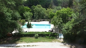A swimming pool surrounded by dense trees, with a wooden deck and lounge chairs. - La Bouriette (Moussoulens)