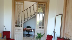 A spacious room with a red sofa, a small table, and a potted plant. A staircase leads to an upper level. - La Bouriette (Moussoulens)