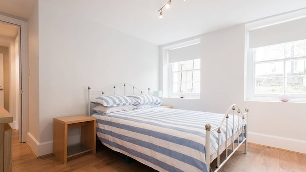 A bedroom with a bed, bedside table, and a window with a view. - The New Kent Road Apartments (London)