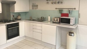 A modern kitchen with white cabinets, a gas stove, a microwave, and a toaster. - The New Kent Road Apartments (London)