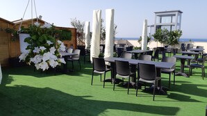 Un espace de restauration en plein air, avec des tables et des chaises, entouré de verdure et de colonnes blanches.