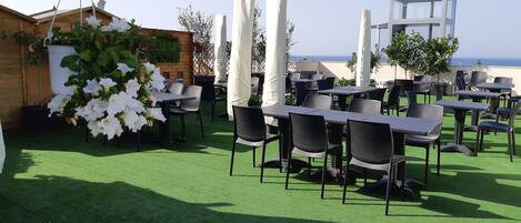 An outdoor dining area with tables and chairs, surrounded by greenery and white columns.