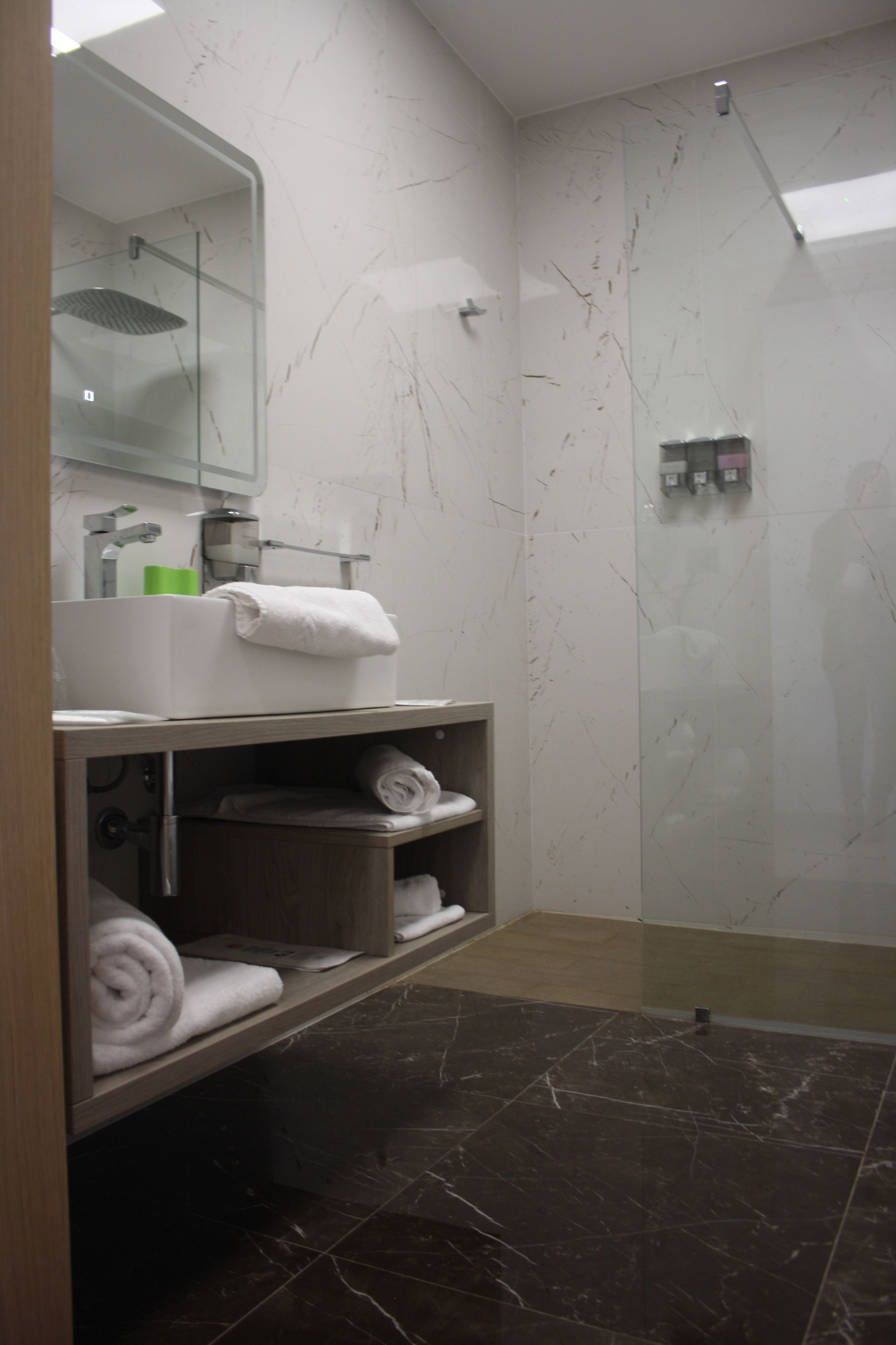 Une salle de bain moderne avec une douche à parois de verre, un meuble-lavabo avec un miroir et des étagères pour ranger les serviettes.