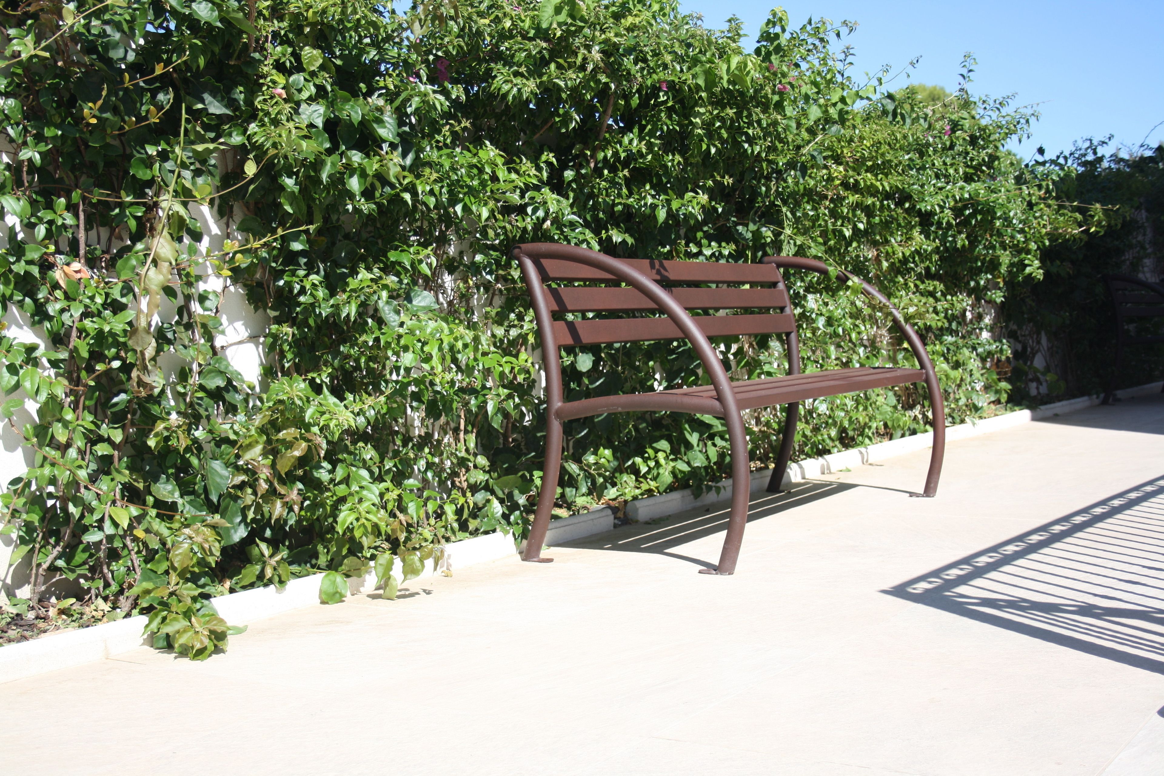 Un banc doté d’un dossier et de deux accoudoirs incurvés, placé sur une surface pavée bordée de blanc.