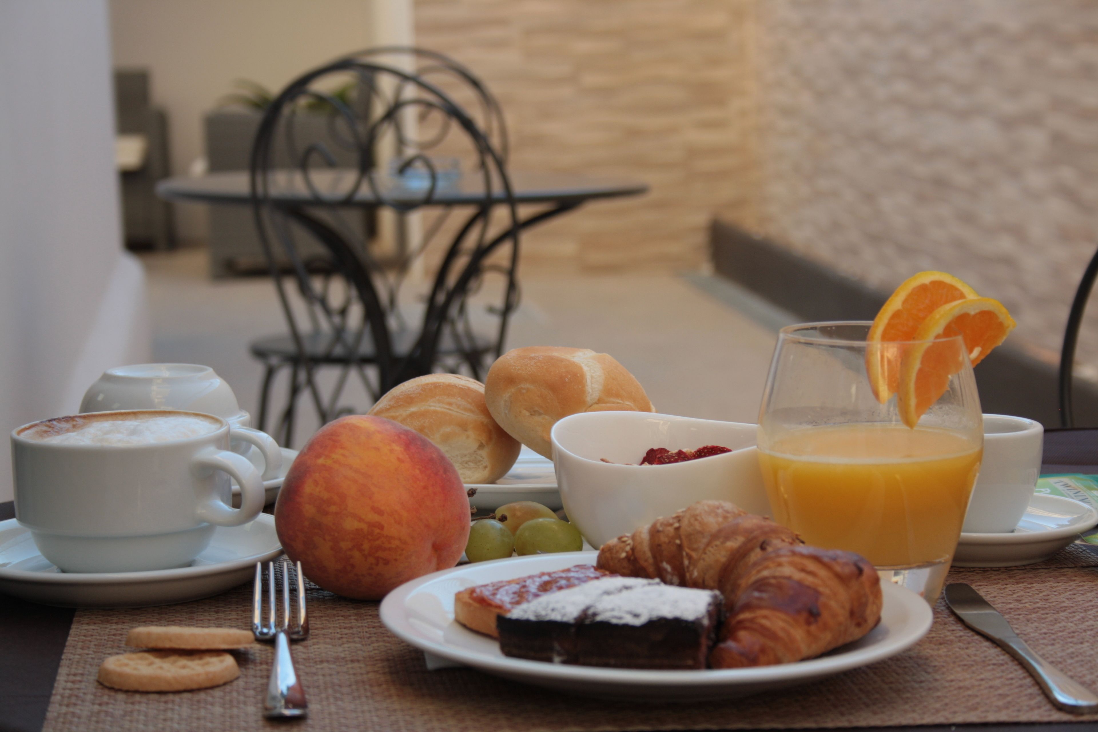 A breakfast setting with croissants, fruit, and a glass of orange juice on a table.