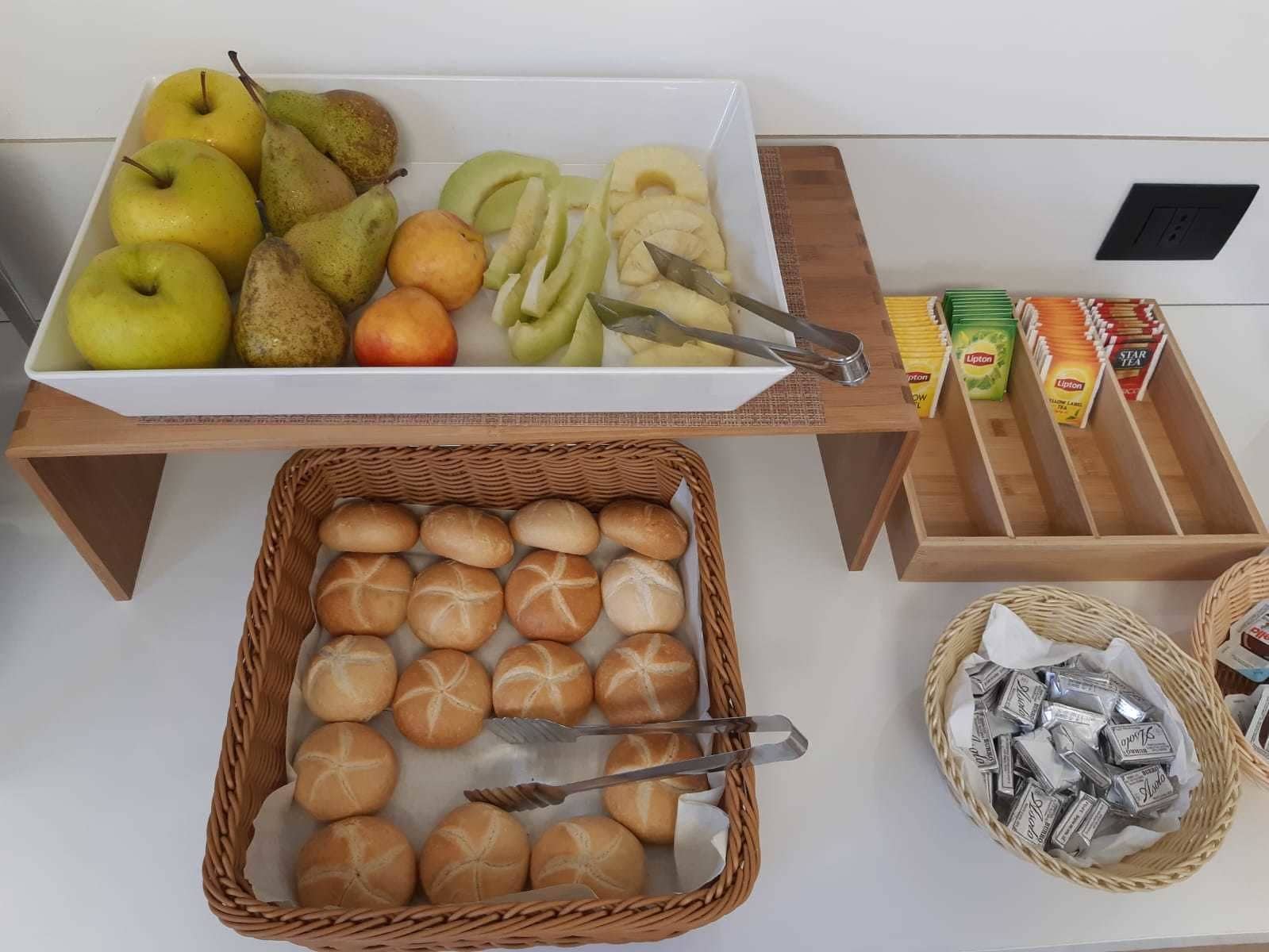 Un tavolo per buffet con frutta assortita, pane e confezioni di tè.
