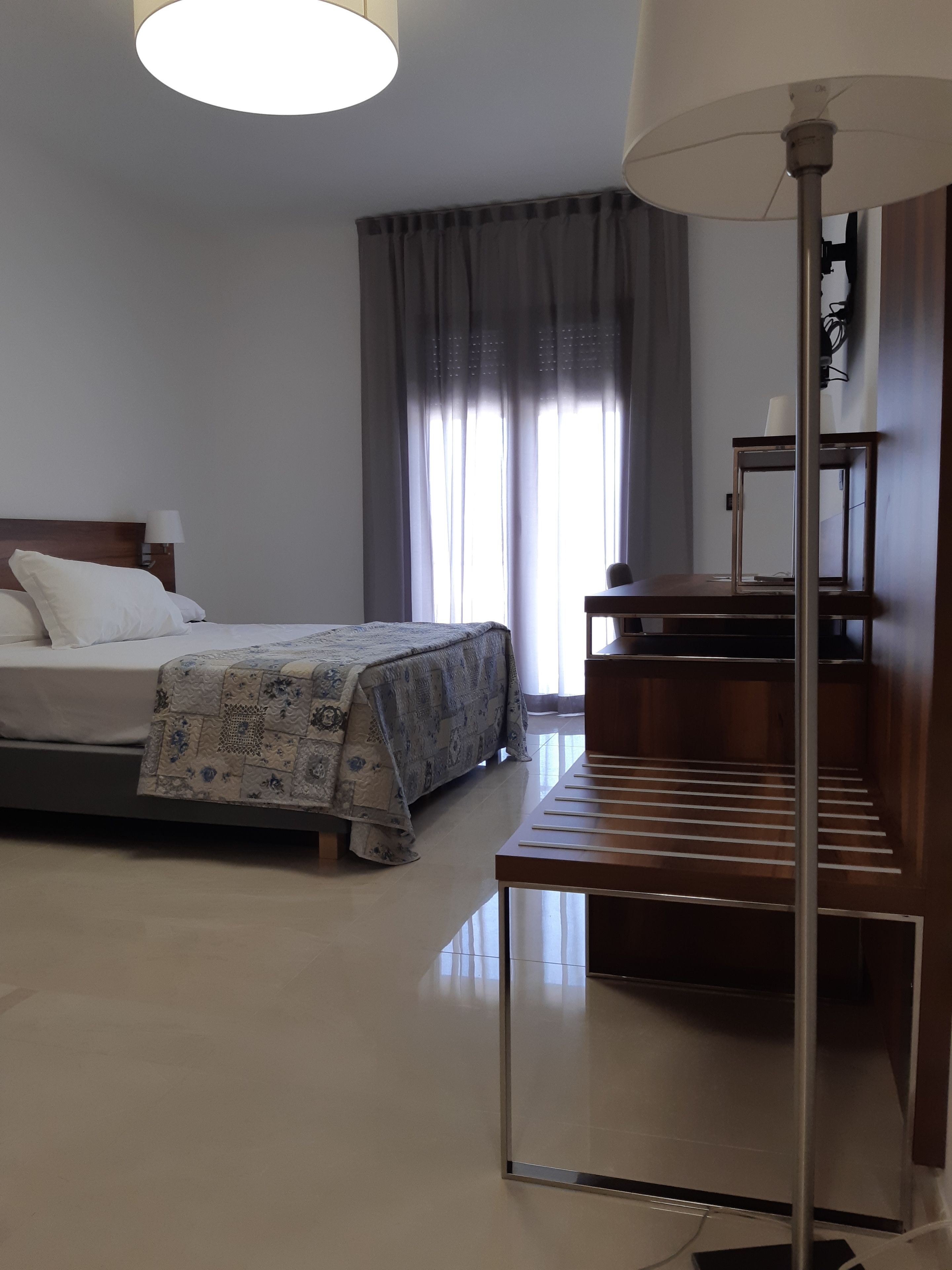 A modern hotel room with a neatly made bed, a desk with a chair, and a large window with curtains.