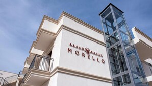 Un hôtel appelé « Morello », doté d’une architecture moderne, se distinguant par une imposante tour de verre et un balcon orné de rampes en métal.