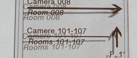 A hotel sign with directions to various rooms and amenities, including camera and room numbers, and an outdoor breakfast room.