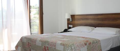 Une chambre d’hôtel avec un grand lit, une table de chevet avec une lampe, une fenêtre avec des rideaux et une vue sur l’extérieur.