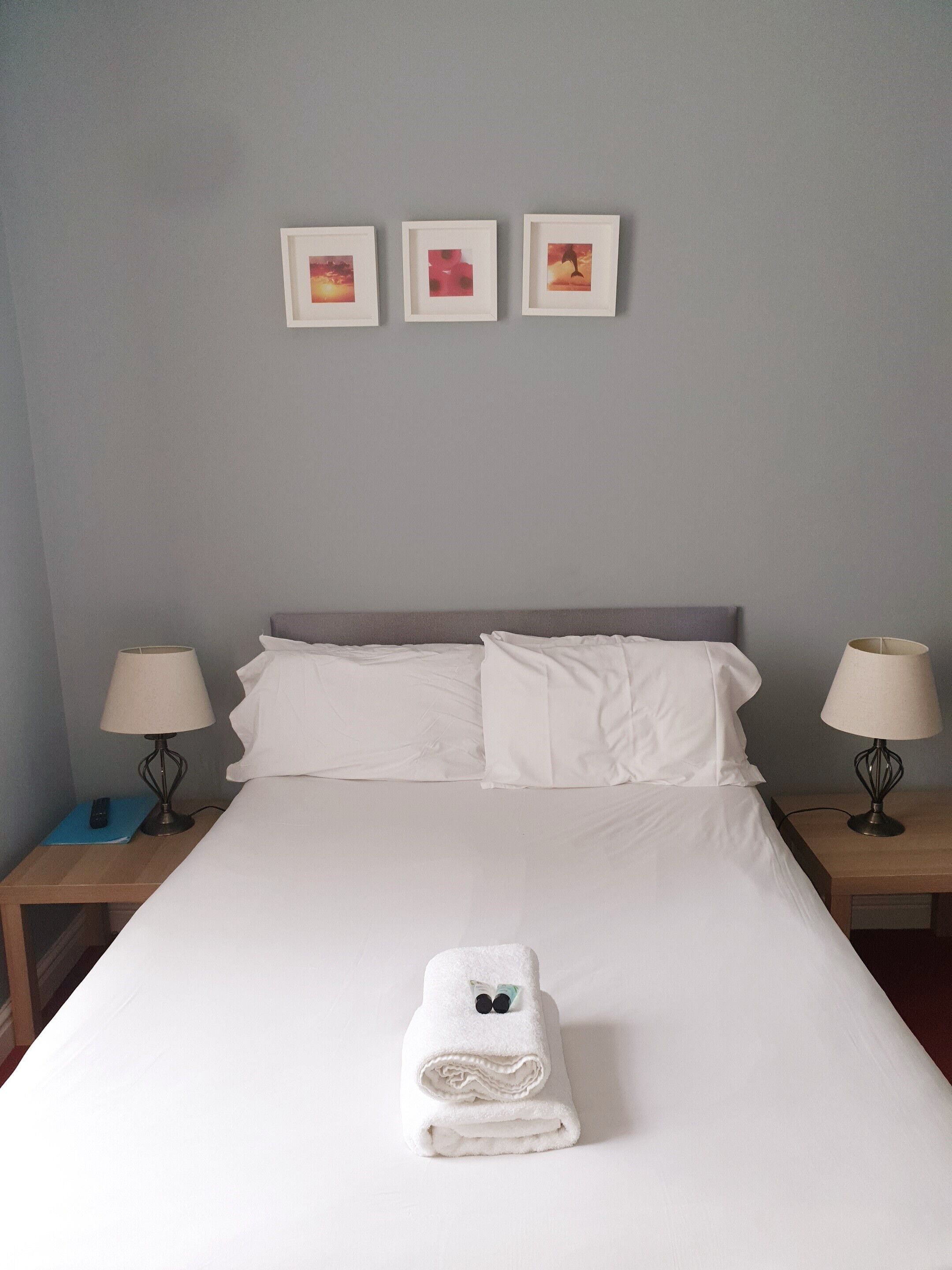 A neatly made bed with white linens, two bedside tables with lamps, and three framed pictures on the wall.