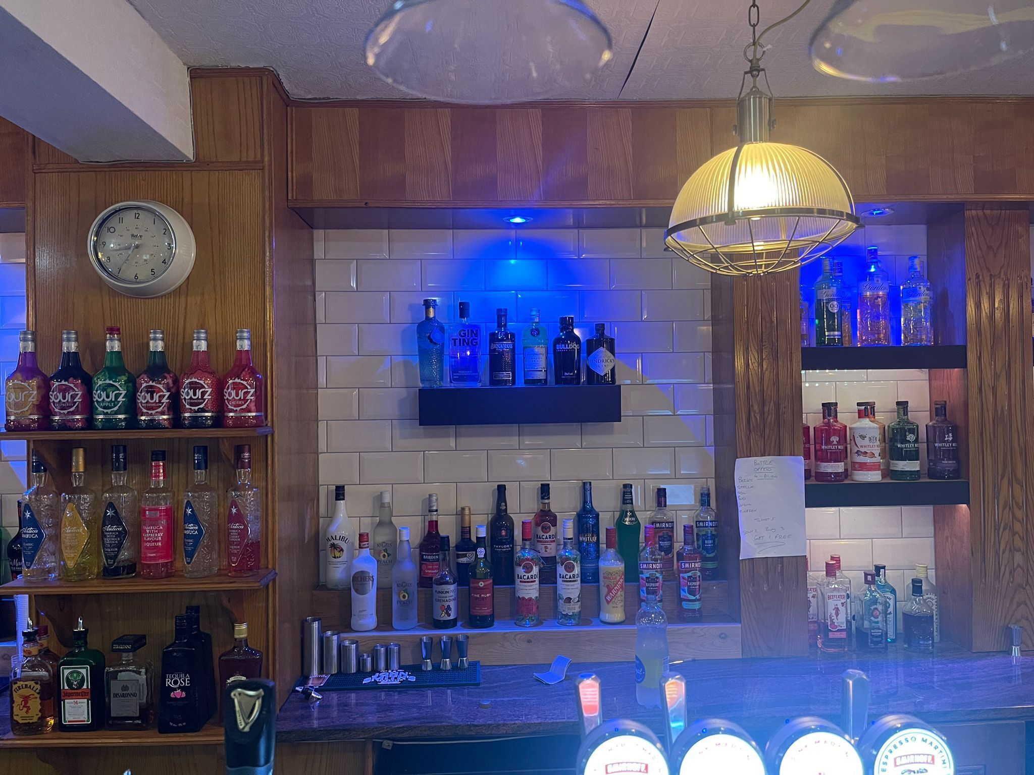 A bar area with shelves of liquor bottles, a clock, and a menu board.