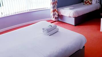 Ein Hotelzimmer mit einem großen Bett, einem kleineren Bett und einem Fenster mit Jalousien.