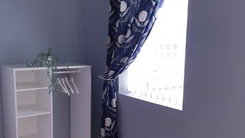 A room with a window, a white shelving unit, and a blue curtain with a leaf pattern.