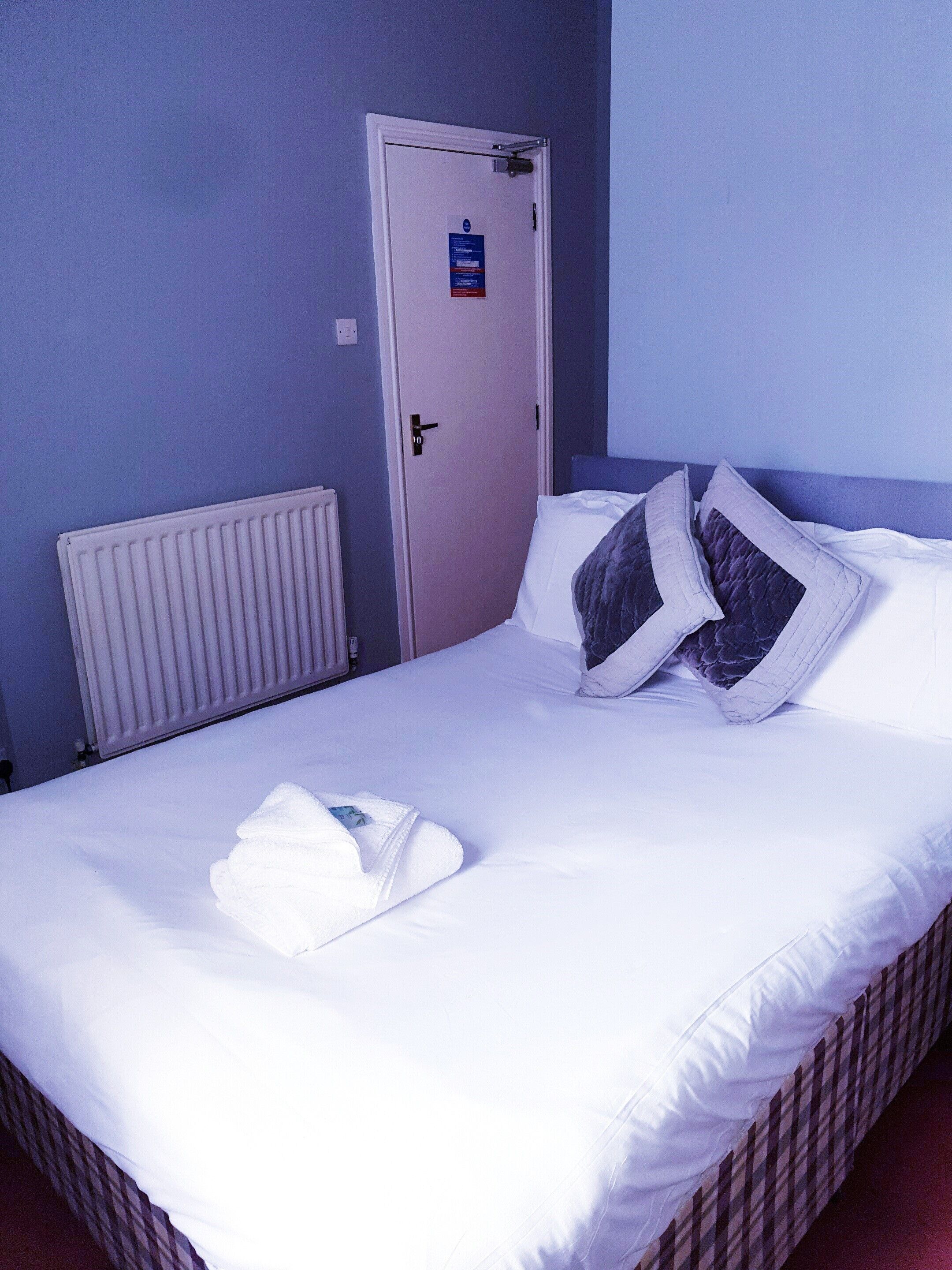 A hotel room with a single bed, white bedding, a white bathrobe, and a door with a sign.