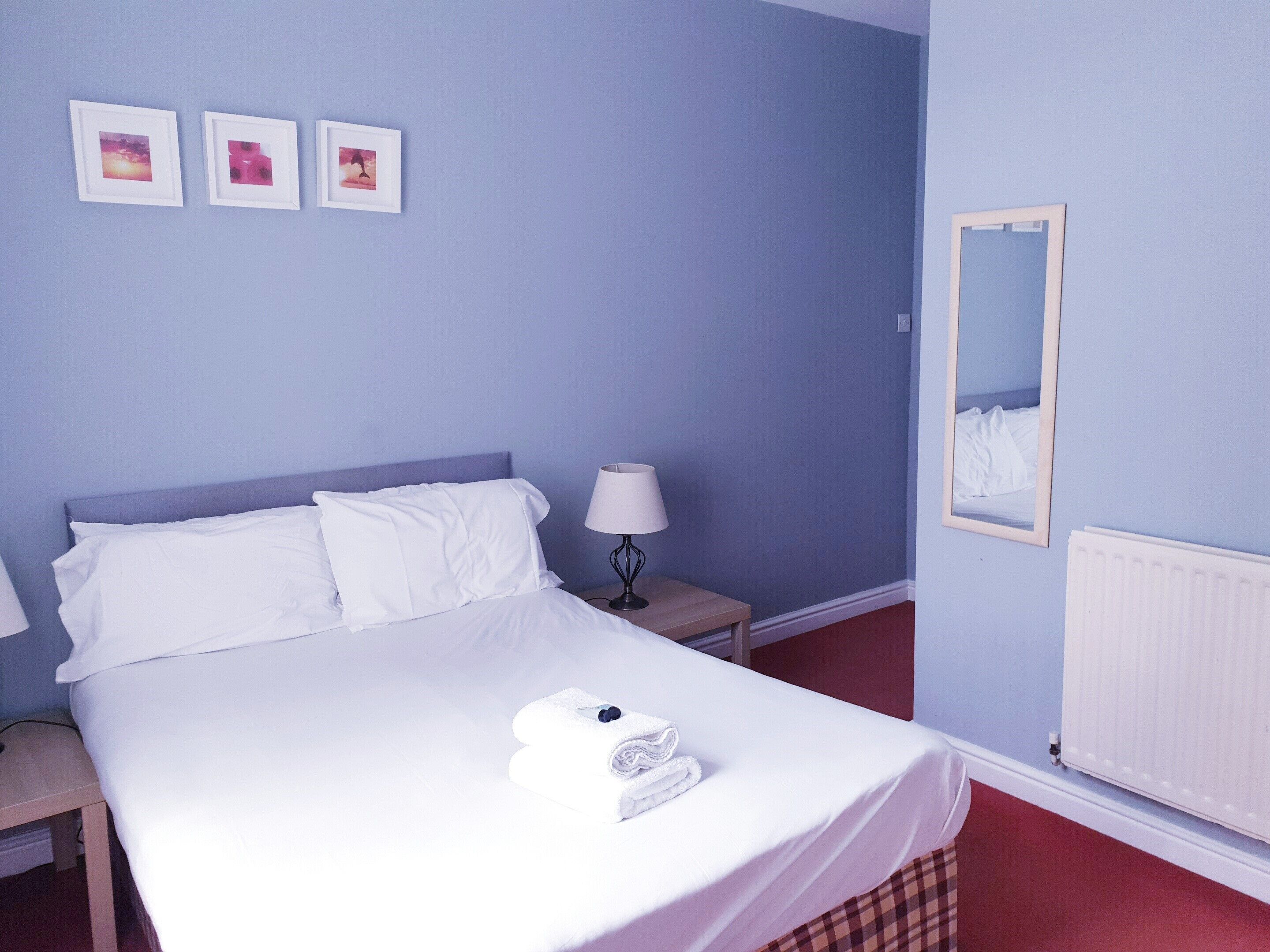 A neatly made bed with white linens, a bedside lamp, and a wall with three framed pictures.