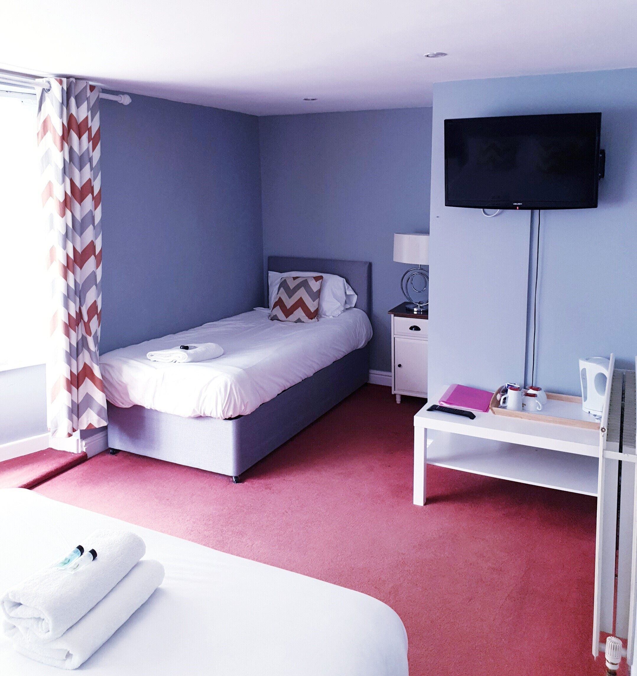 A modern hotel room with a bed, a desk, a TV, and a window with curtains.