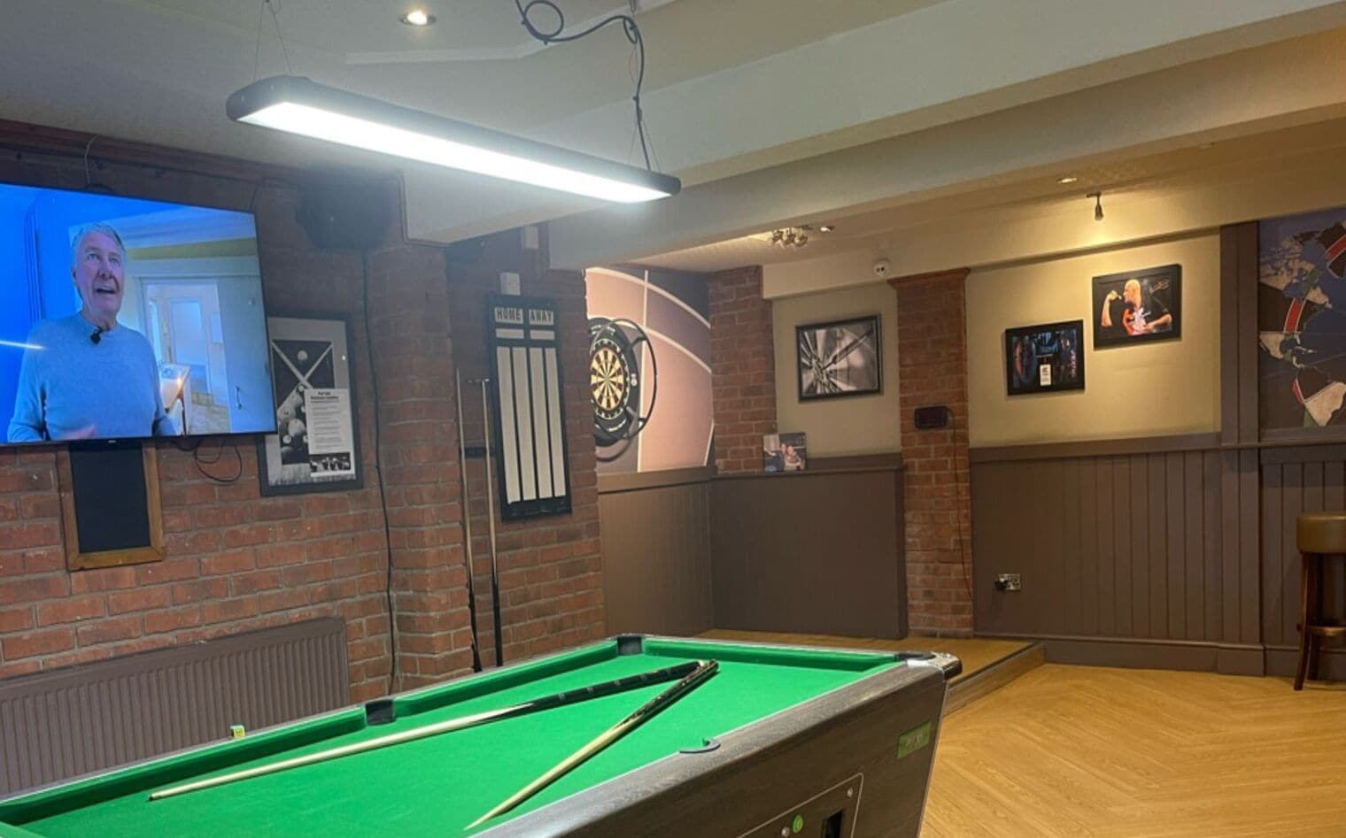 A billiards room with a pool table, dartboard, and a television screen.