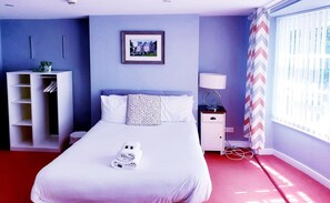 A neatly made bed with a folded towel, a bedside table with a lamp, a framed picture on the wall, and a wardrobe with hanging clothes. - The Grey Horse (Darlington)