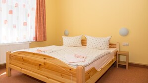 Habitación individual con una cama que tiene cabecera de madera, una mesita de noche pequeña y un ventanal con cortinas.