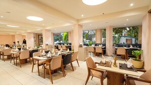 A spacious dining area with multiple tables and chairs, large windows, and a view of the outside. - Hotel Mayura (Raipur)