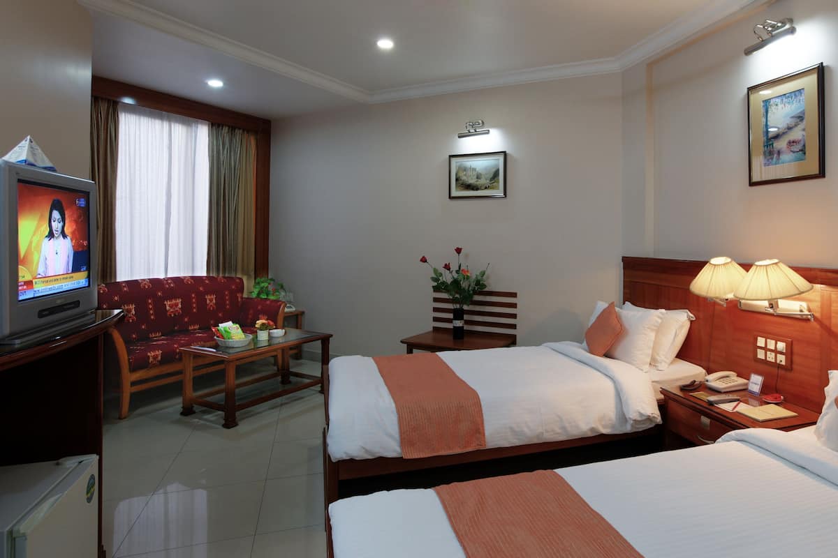 A hotel room with two beds, a television, a desk with a lamp, and a painting on the wall.