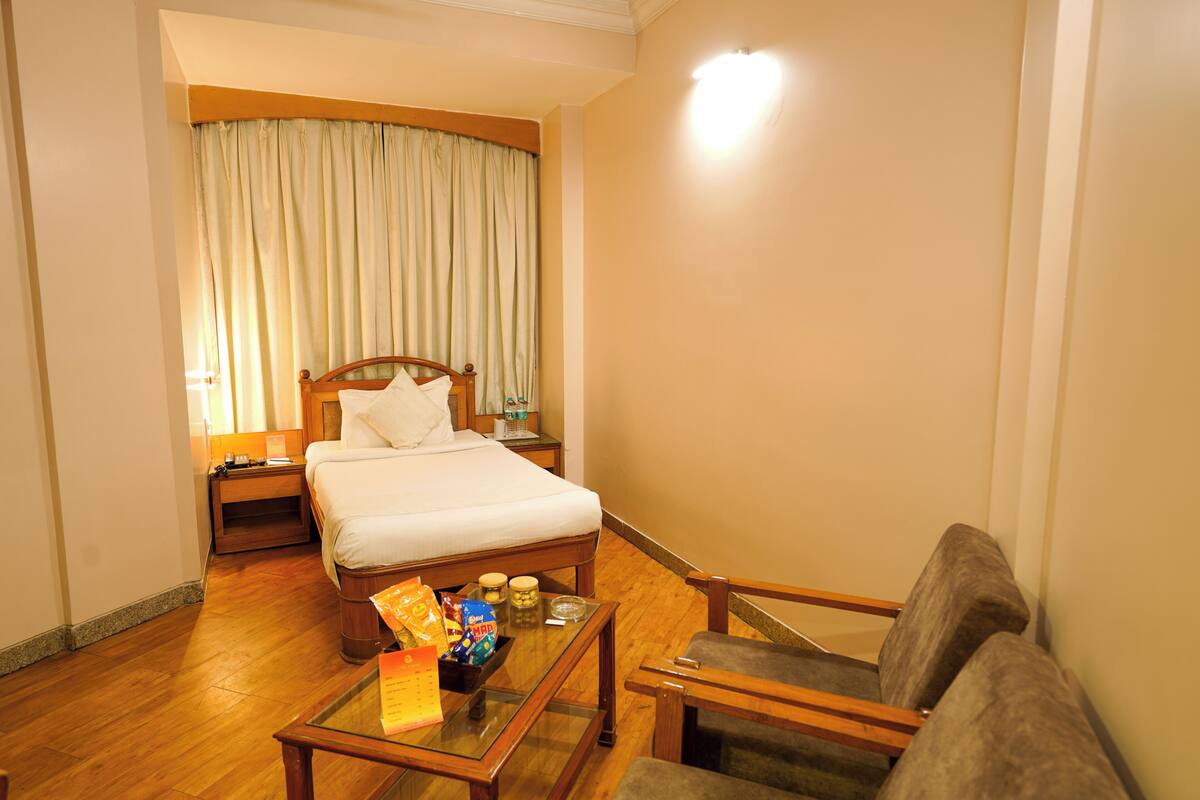 A hotel room with a bed, a nightstand, a glass-top table with snacks, and a sofa.