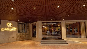 A hotel entrance with a wooden ceiling, a neon sign, and a tiled floor. - Hotel Mayura (Raipur)
