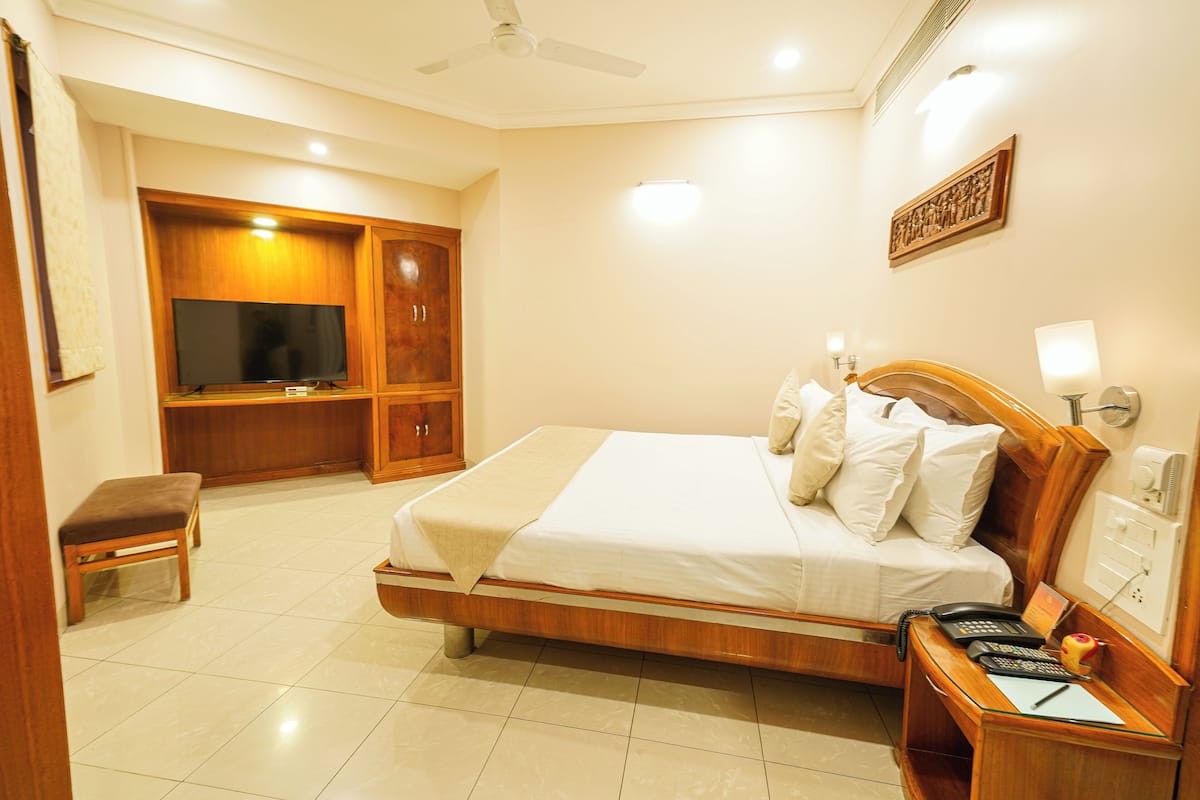 A hotel room with a bed, bedside table, desk, television, wardrobe, and a bench.