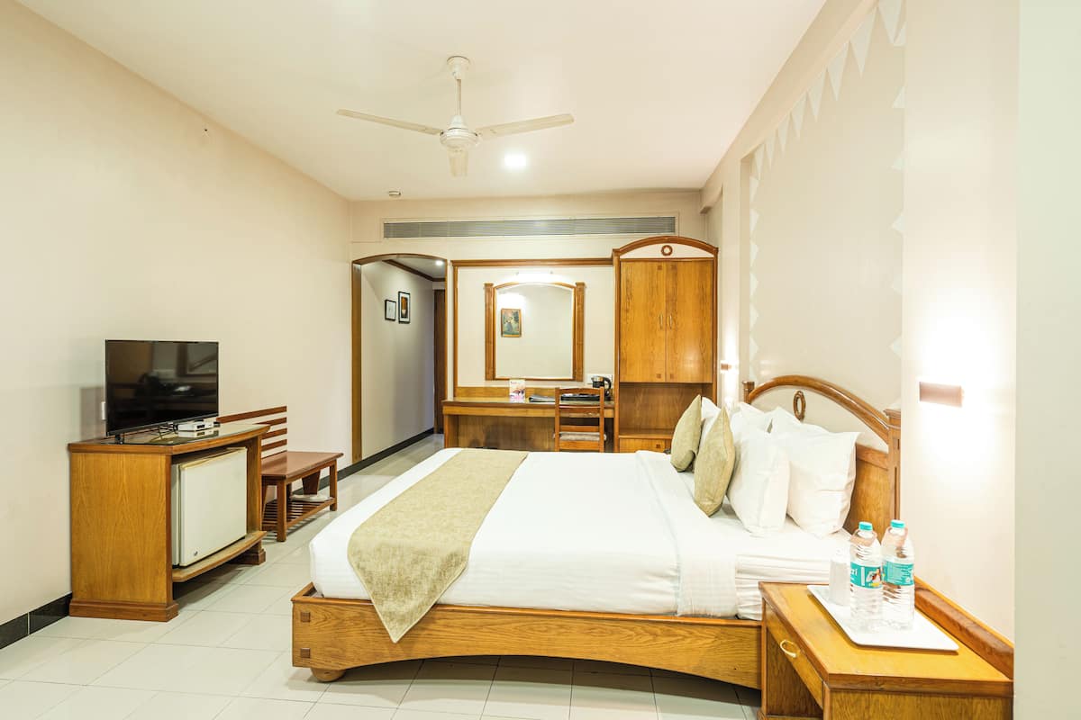 A hotel room with a bed, a desk, a television, a wardrobe, and a mirror.