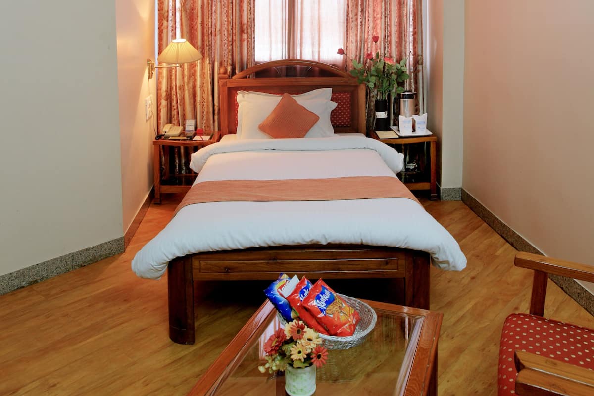 A hotel room with a bed, bedside table, lamp, and a small table with snacks and a vase.