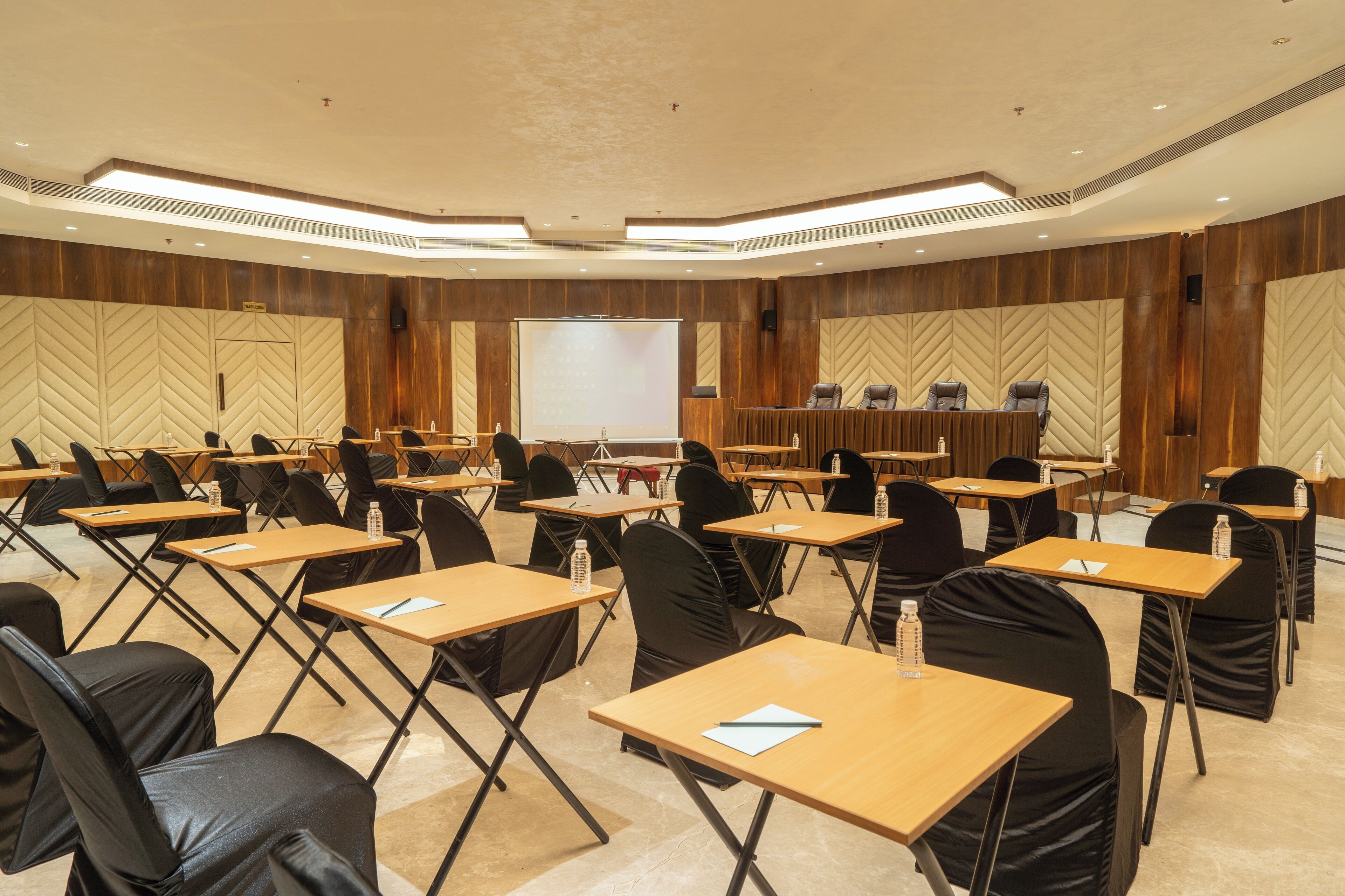 A conference room with multiple tables and chairs, a large screen, and a podium.