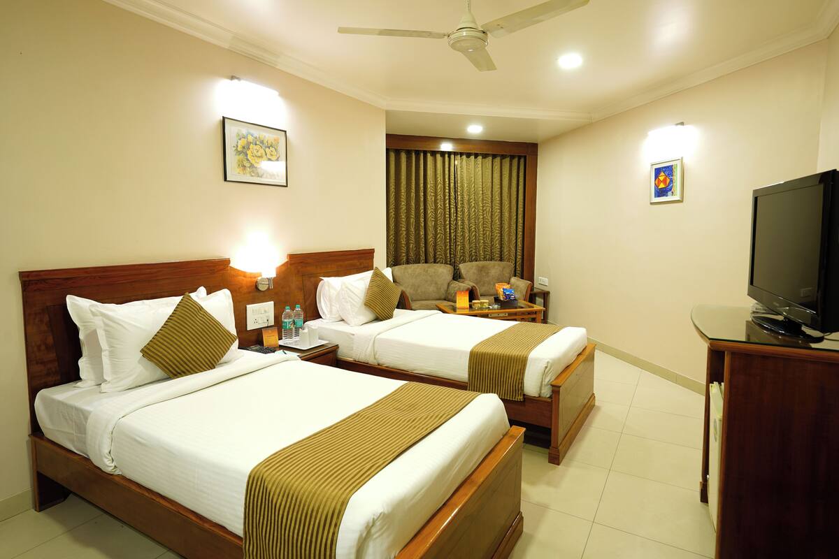 A hotel room with two beds, a television, a ceiling fan, and a curtain backdrop.