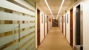 A hotel corridor with a carpeted floor, glass partitions, and doors leading to rooms. - Hotel Mayura (Raipur)