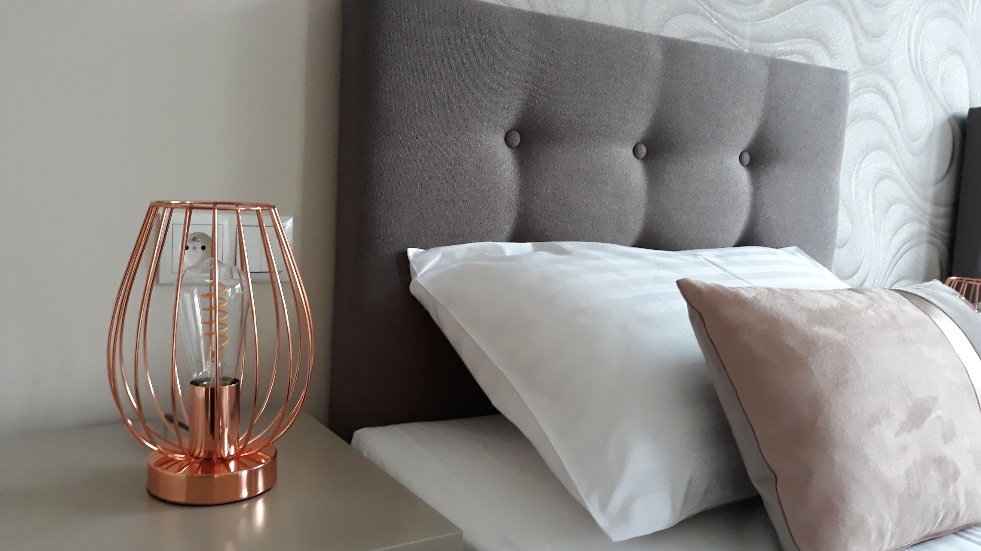 A neatly made bed with a grey upholstered headboard, a white pillow, and a beige pillow.