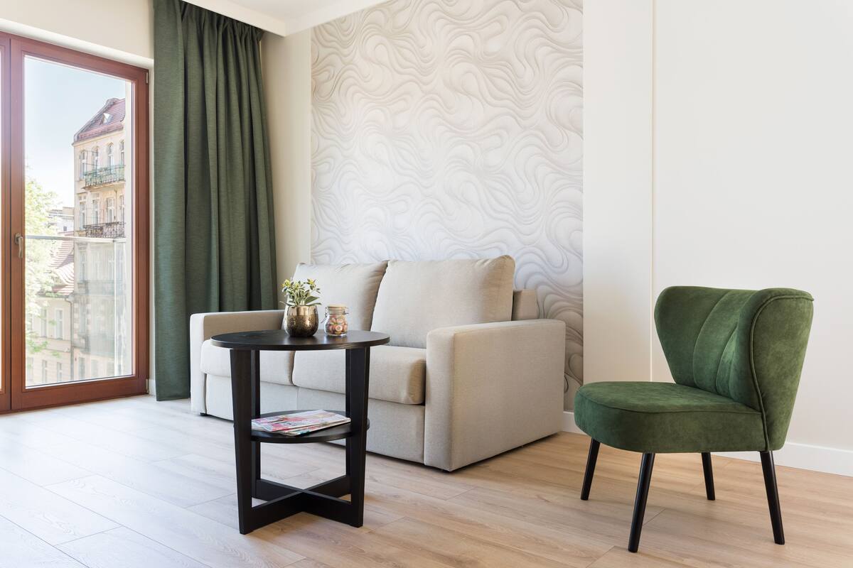 A modern living room with a sofa, a green armchair, a small table with a plant, and a patterned wall.