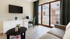 Uma sala de estar moderna com uma televisão de tela plana, uma escrivaninha com um laptop, uma cadeira verde, um sofá e uma janela grande com vista para um edifício.