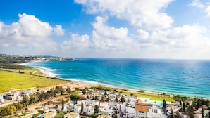 A coastal town with a beach, clear blue sea, and white buildings with red roofs. - Villa Siena (Pegeia)