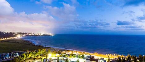 Un pueblo costero con playa, edificios iluminados y una vista despejada del mar.