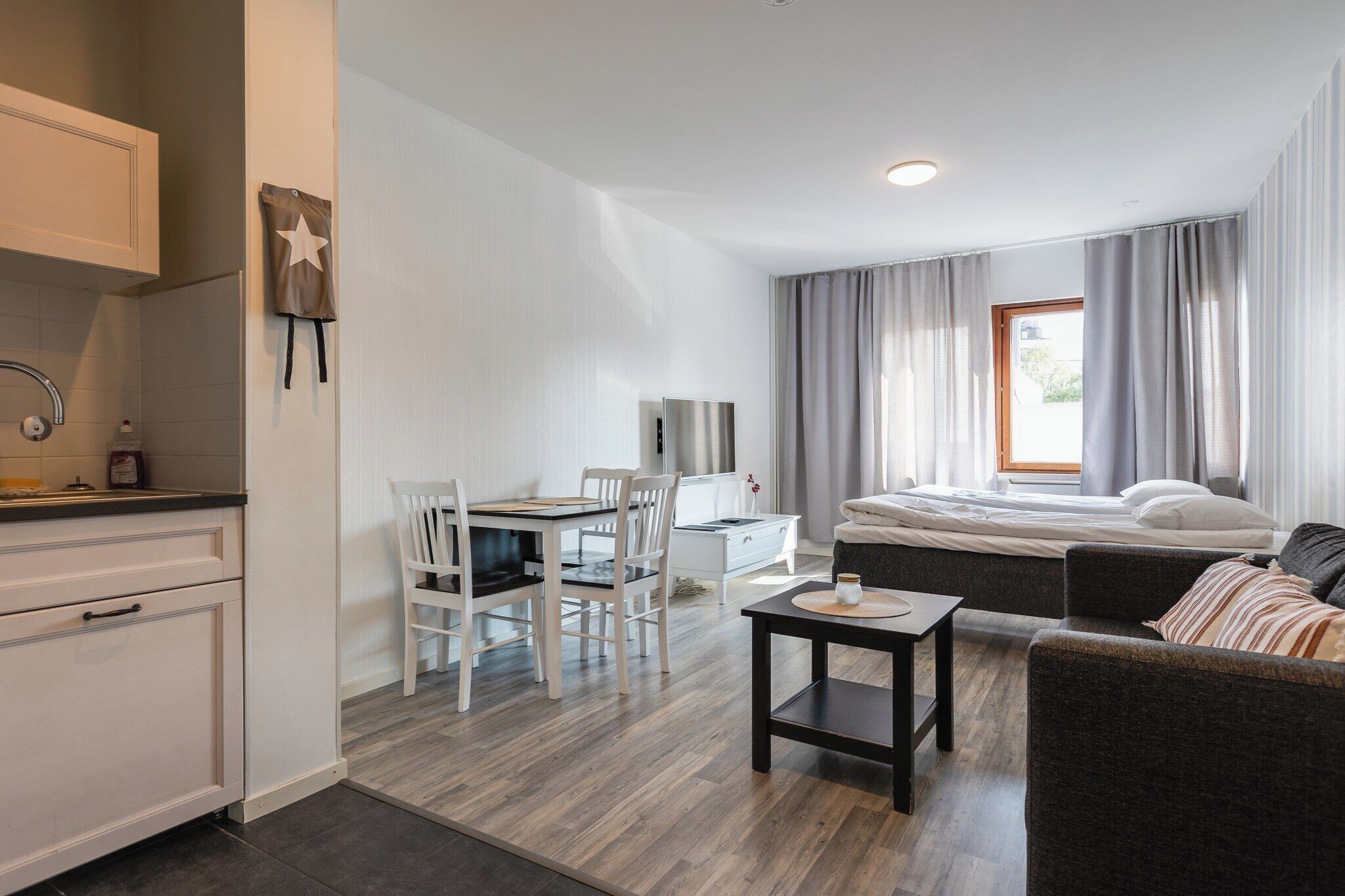 Ein modernes, helles Zimmer mit Küchenzeile, Essbereich, Bett und Sitzecke.