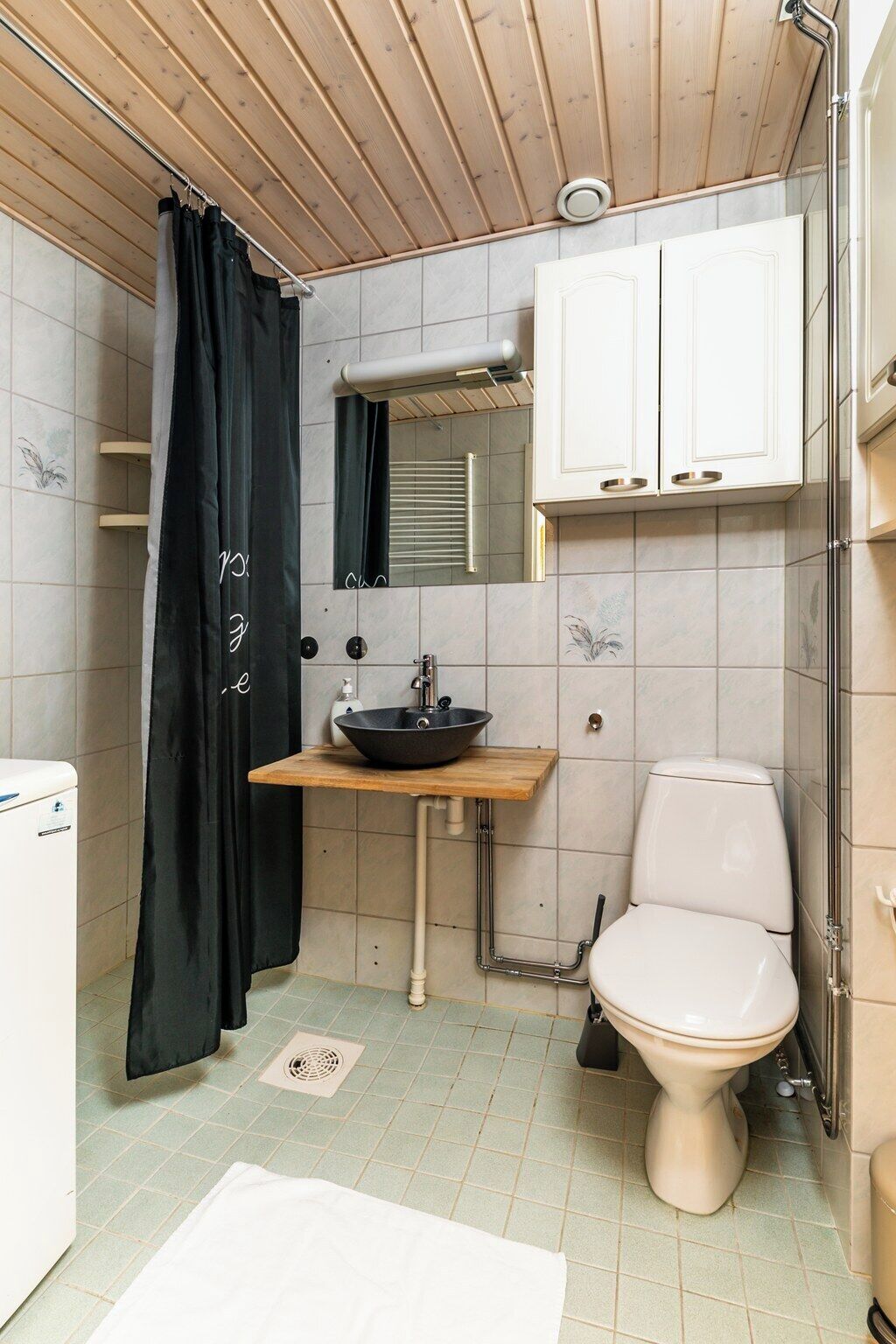 A compact bathroom with a wooden ceiling, a black bathtub, a white toilet, and a wooden vanity with a sink.