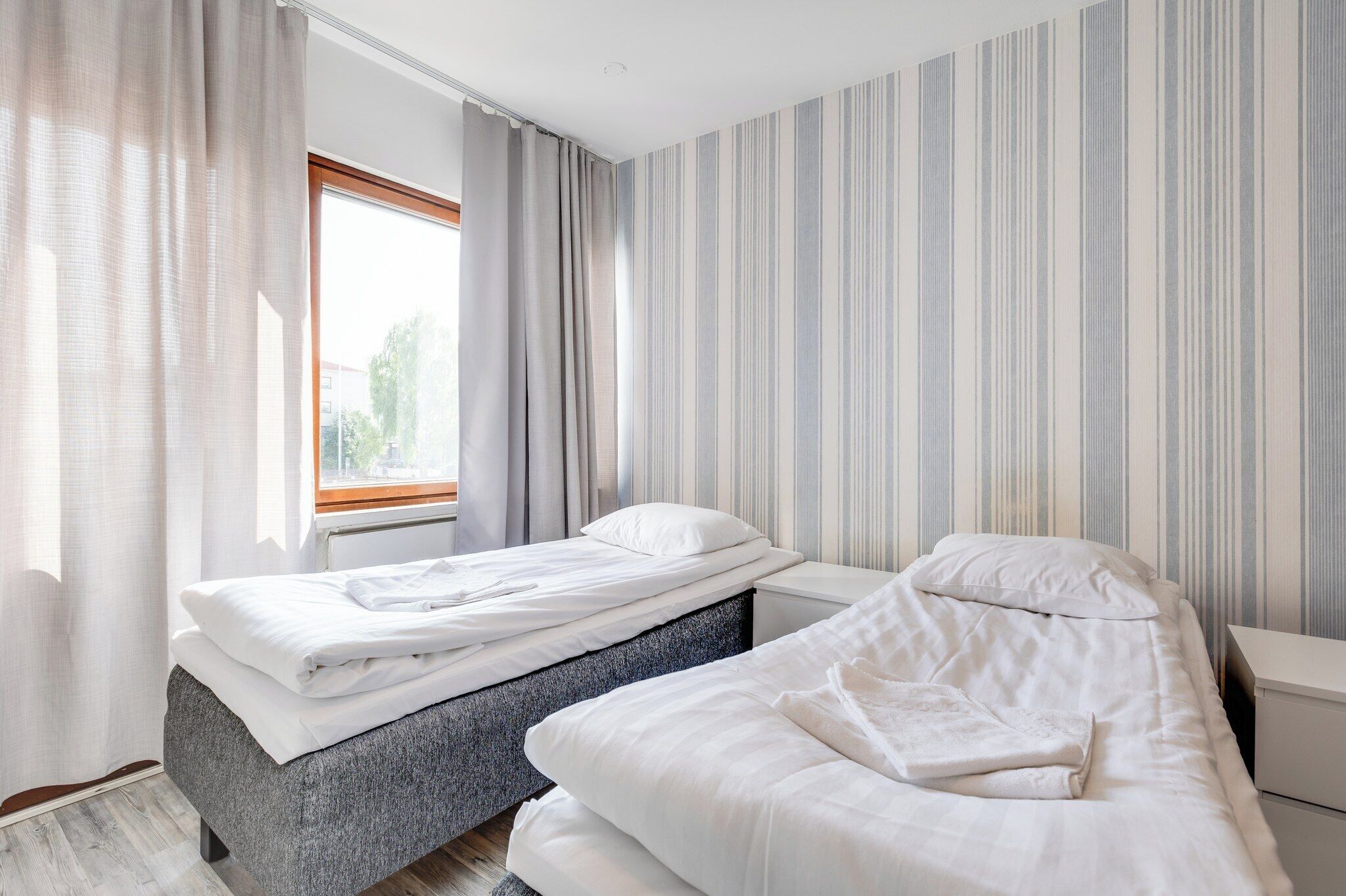 A bedroom with two beds, a window with curtains, and striped wallpaper.