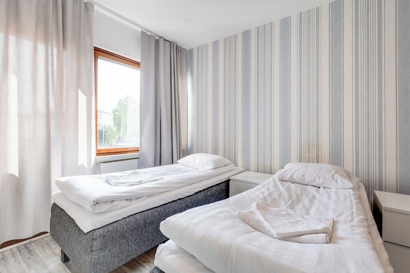 Un dormitorio con dos camas, una ventana con cortinas y papel tapiz a rayas.
